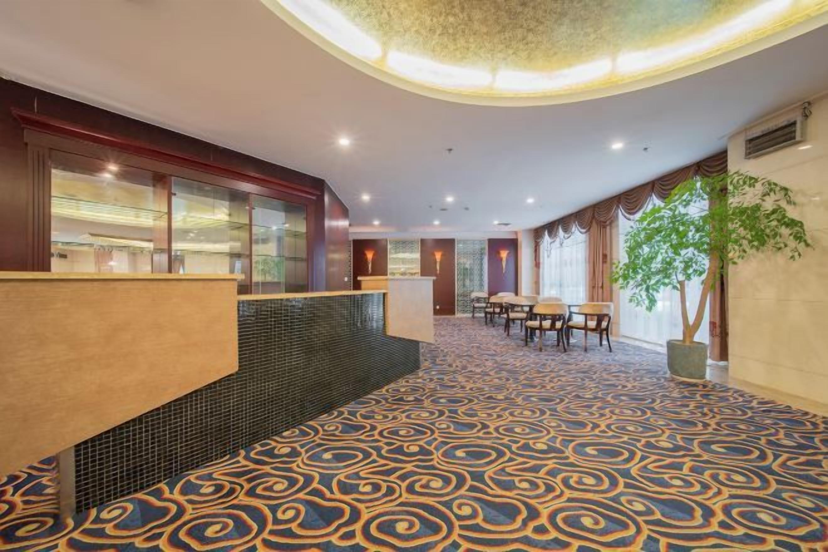 A hotel lobby with a patterned carpet, a reception desk, and a seating area.