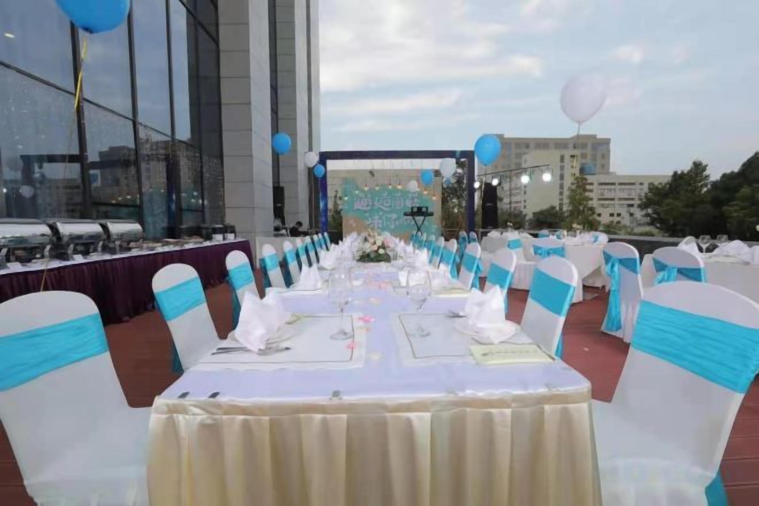 An outdoor banquet setup with tables and chairs, a stage, and a view of a building in the background.