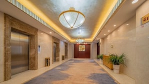 Un pasillo de hotel con piso de mármol, dos ascensores y una puerta de madera al final.