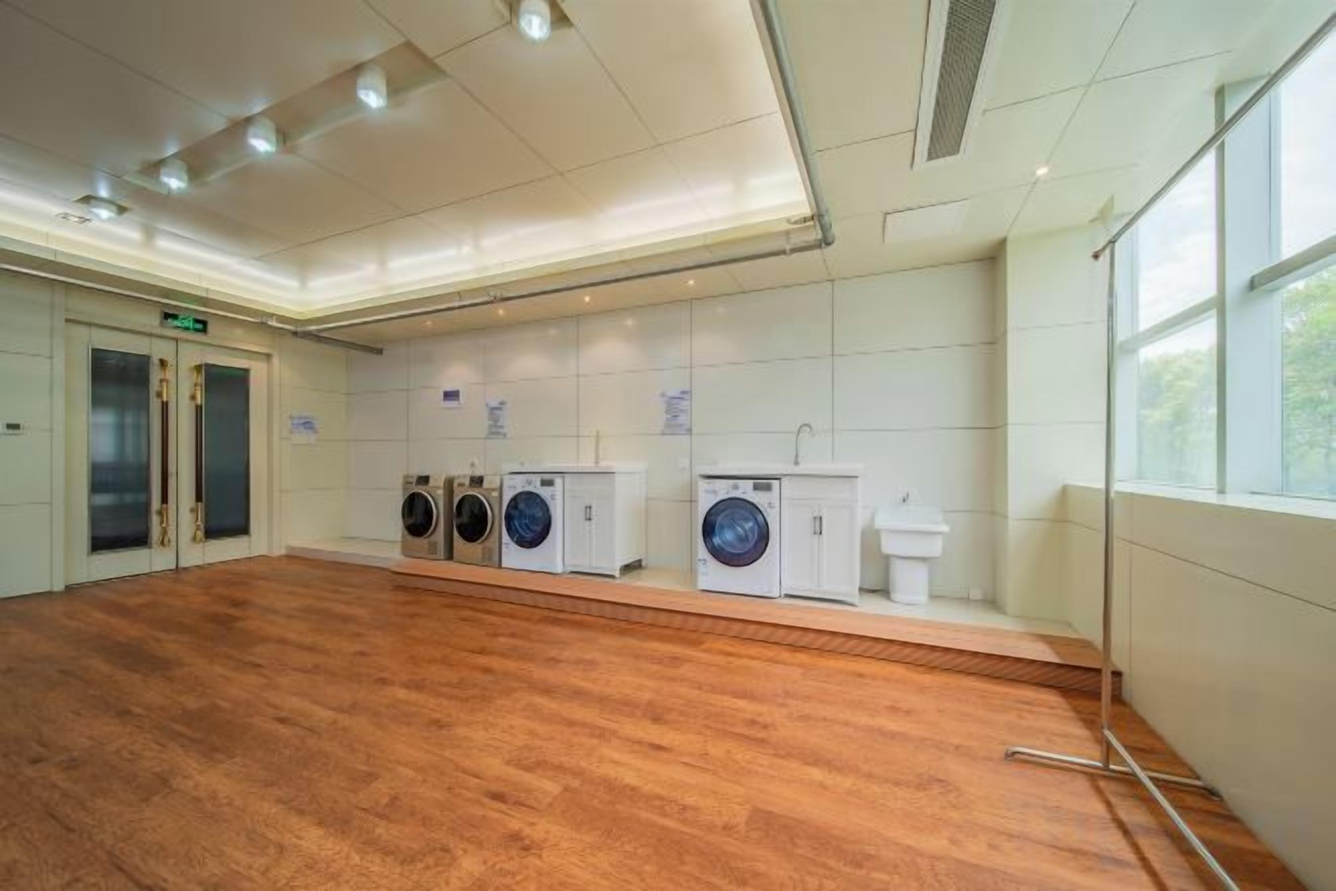 A laundry facility with multiple washing machines and dryers, a sink, and a wooden floor.