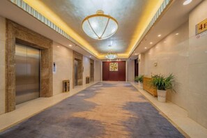 A hotel corridor with elevators, a reception desk, and potted plants. - Anhui International Hotel (Nantong)