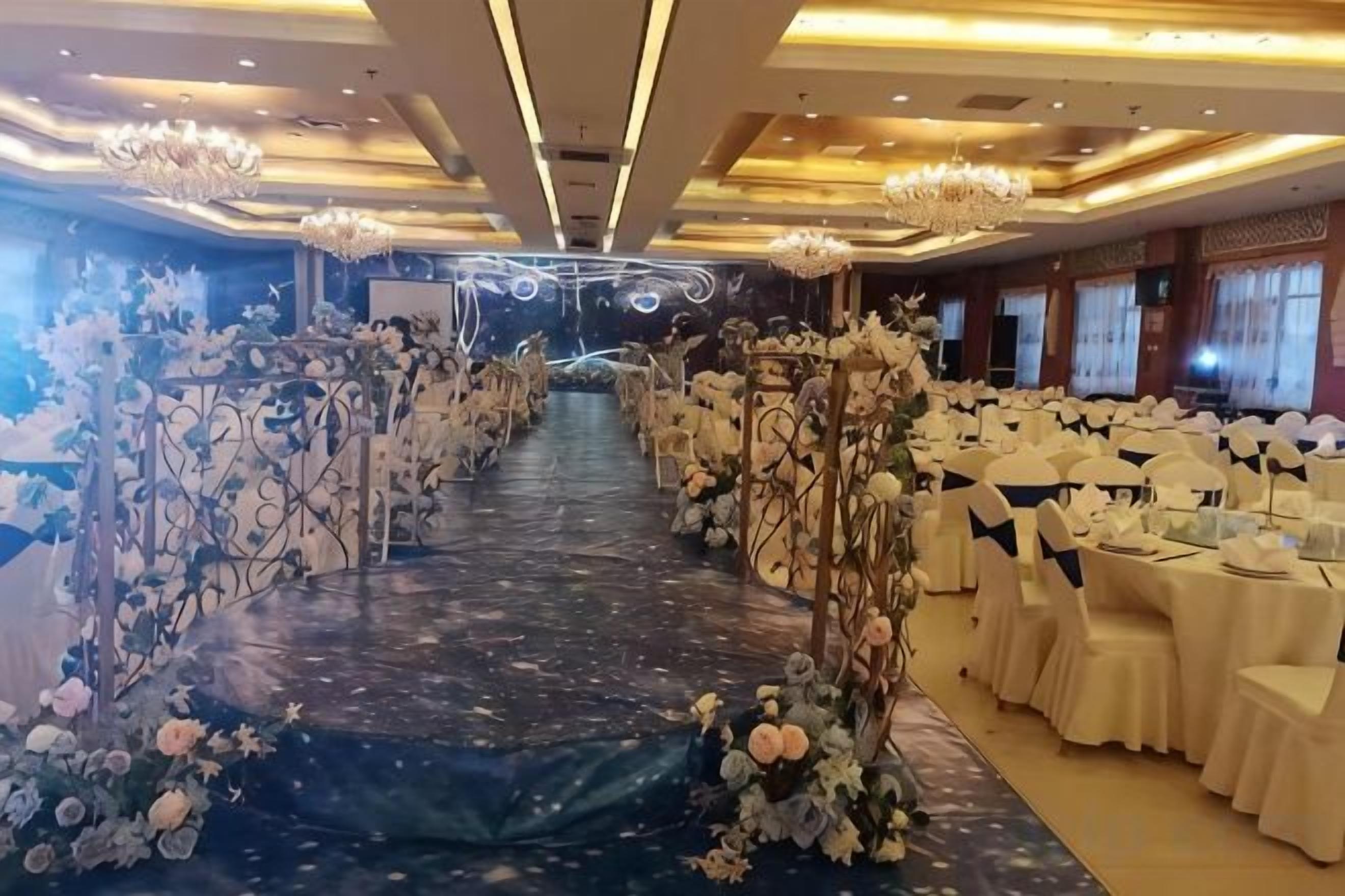 Un salón de banquetes con un pasillo central, mesas a ambos lados y decoración floral.