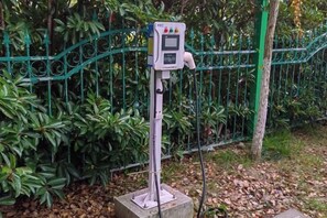 Un parquímetro con pantalla digital, situado en una zona ajardinada con valla metálica y vegetación.
