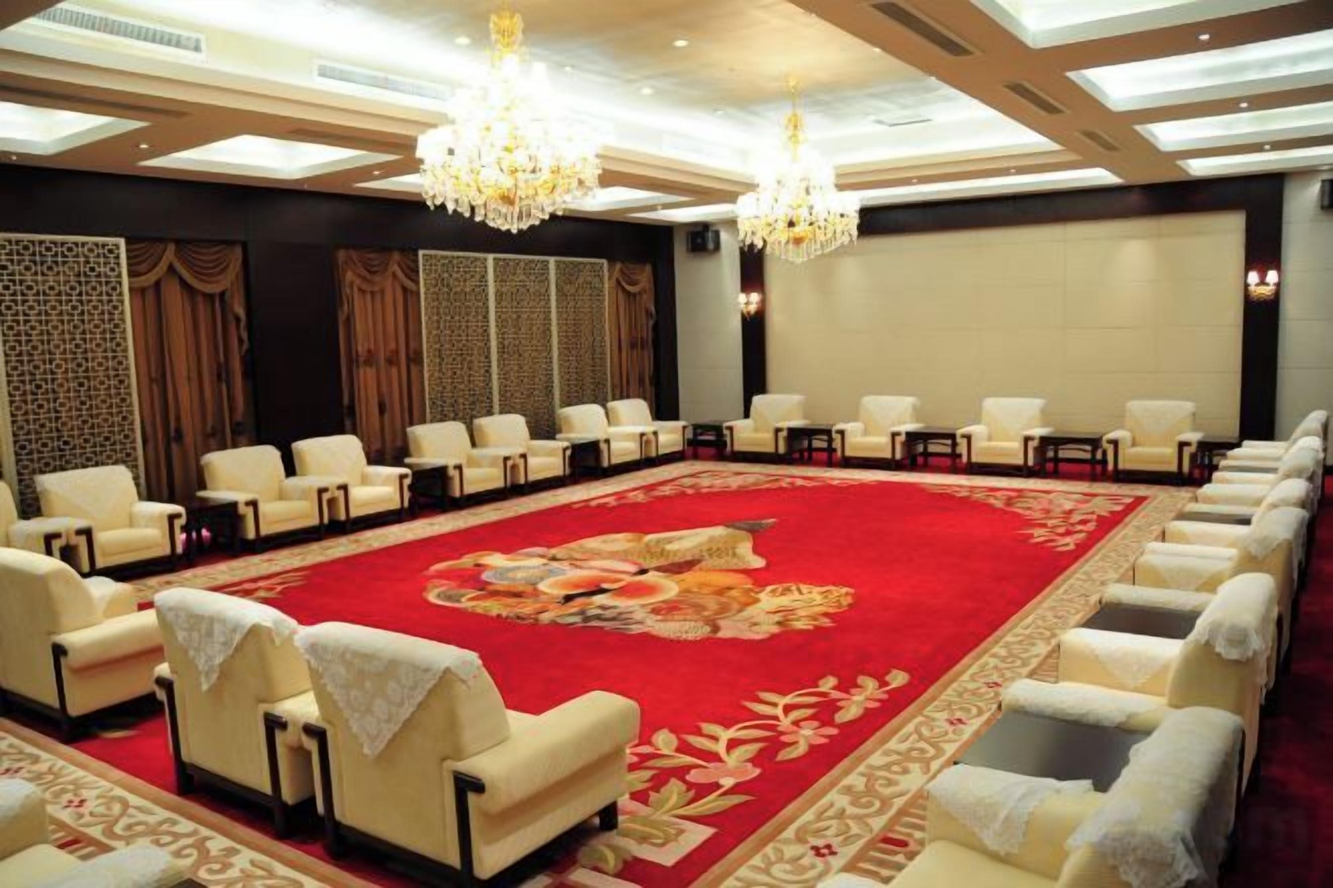 A conference room with rows of chairs, a red carpet, and chandeliers.