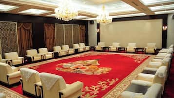 A conference room with rows of chairs, a red carpet, and chandeliers.
