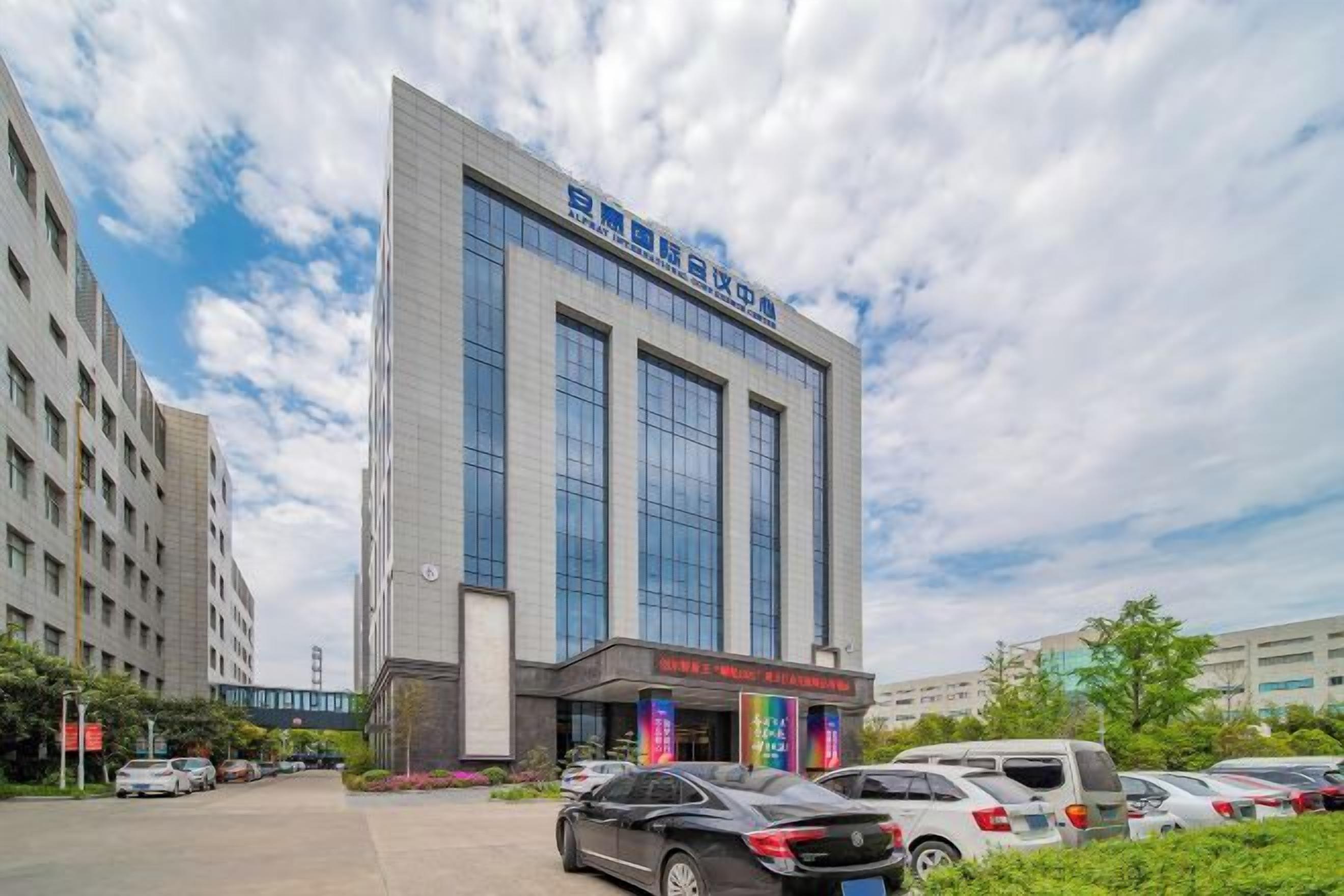 A modern building with a large glass facade, a parking lot, and a clear sky.