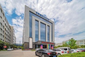 A modern building with a large glass facade, a parking lot, and a clear sky. - Anhui International Hotel (Nantong)