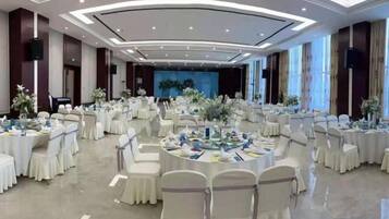 A banquet hall with round tables, white chairs, and floral centerpieces.