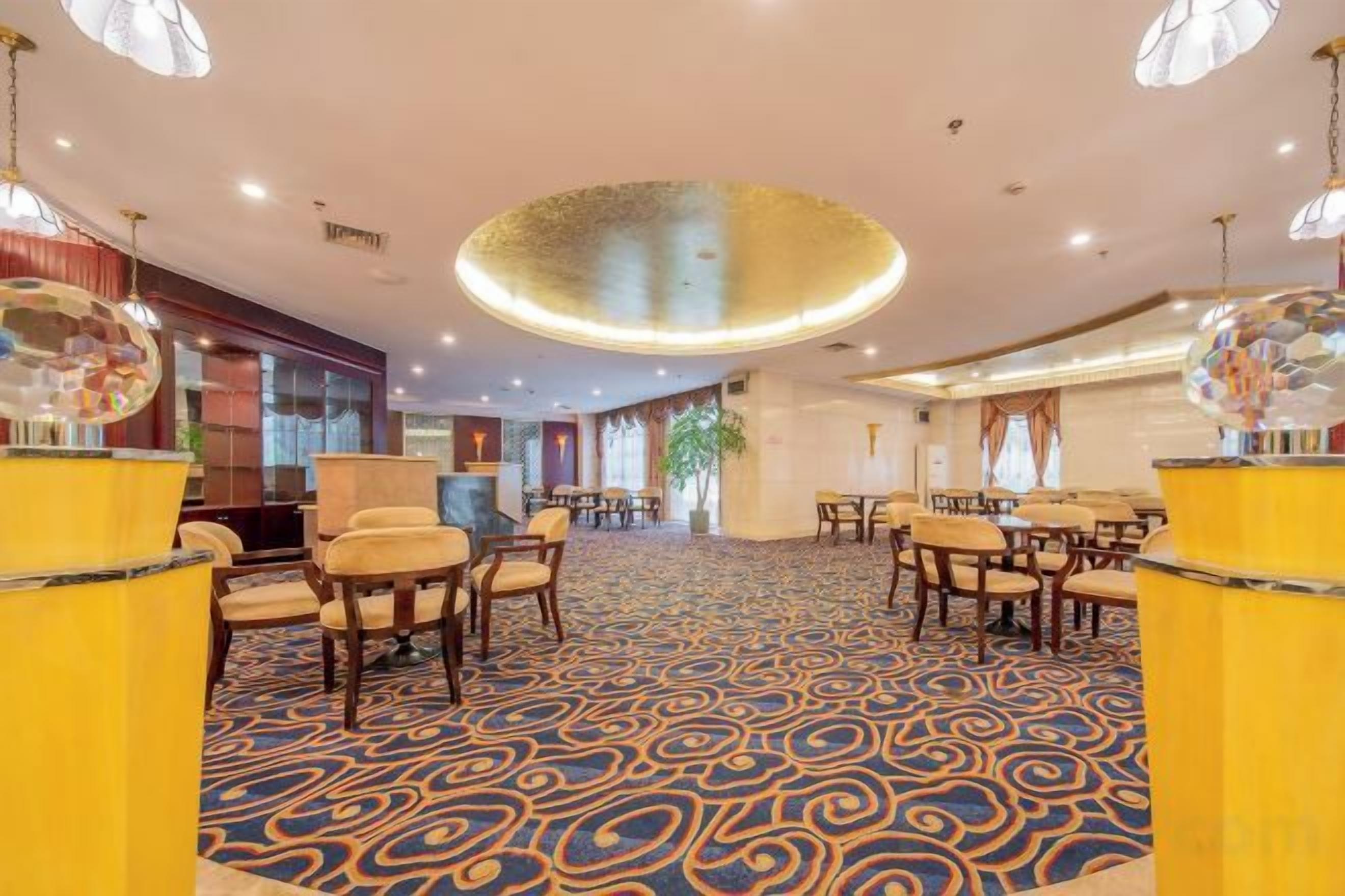 Un vestíbulo de hotel con alfombra estampada, mesas redondas y sillas.