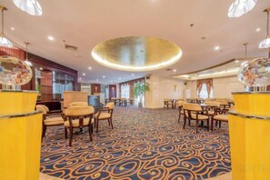 Un hall d’hôtel avec un tapis à motifs, des tables rondes et des chaises.