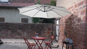 Un patio con una mesa, sillas, un paraguas grande y un carrito pequeño.
