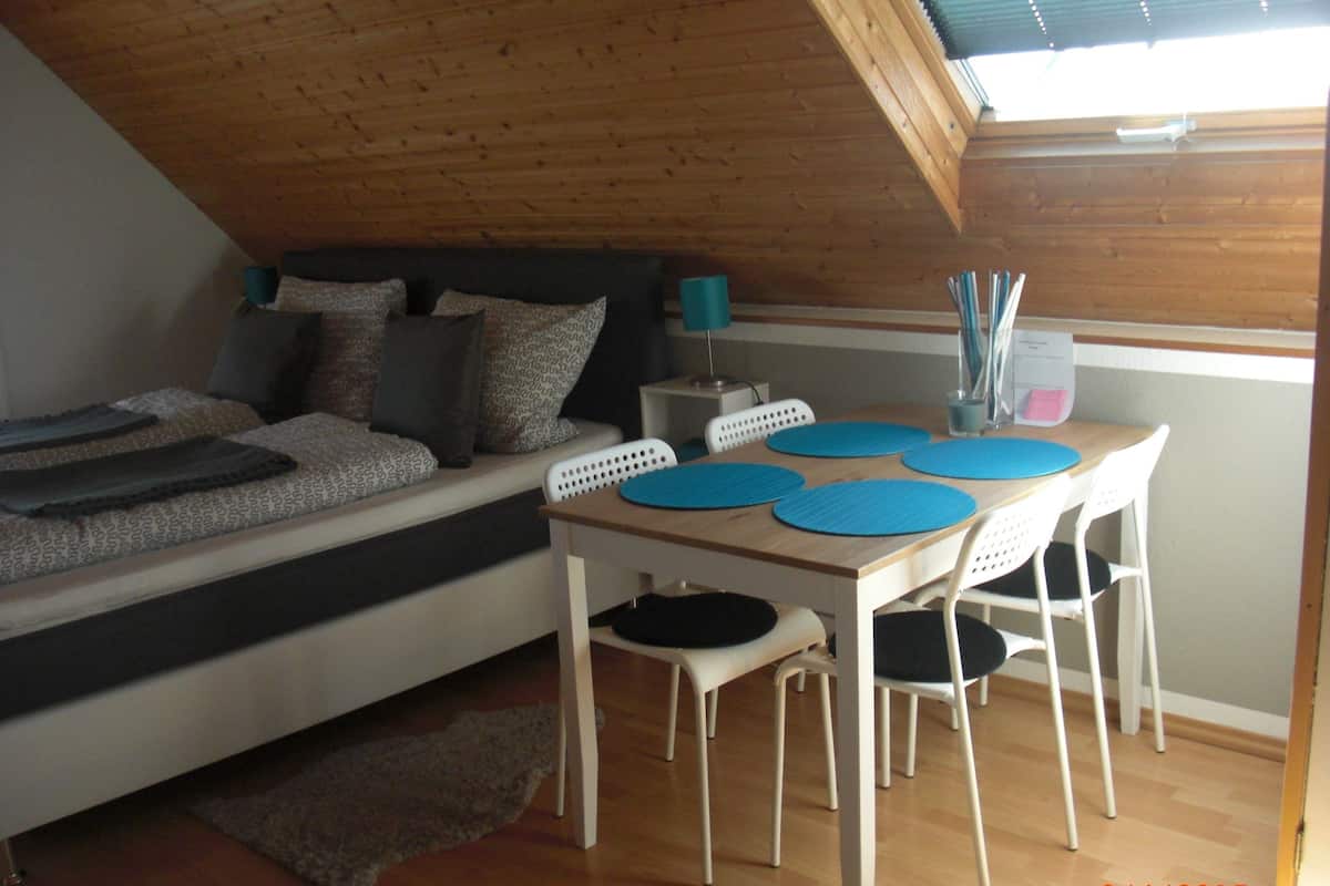 A loft bedroom with a bed, a dining table with chairs, and a small desk area.