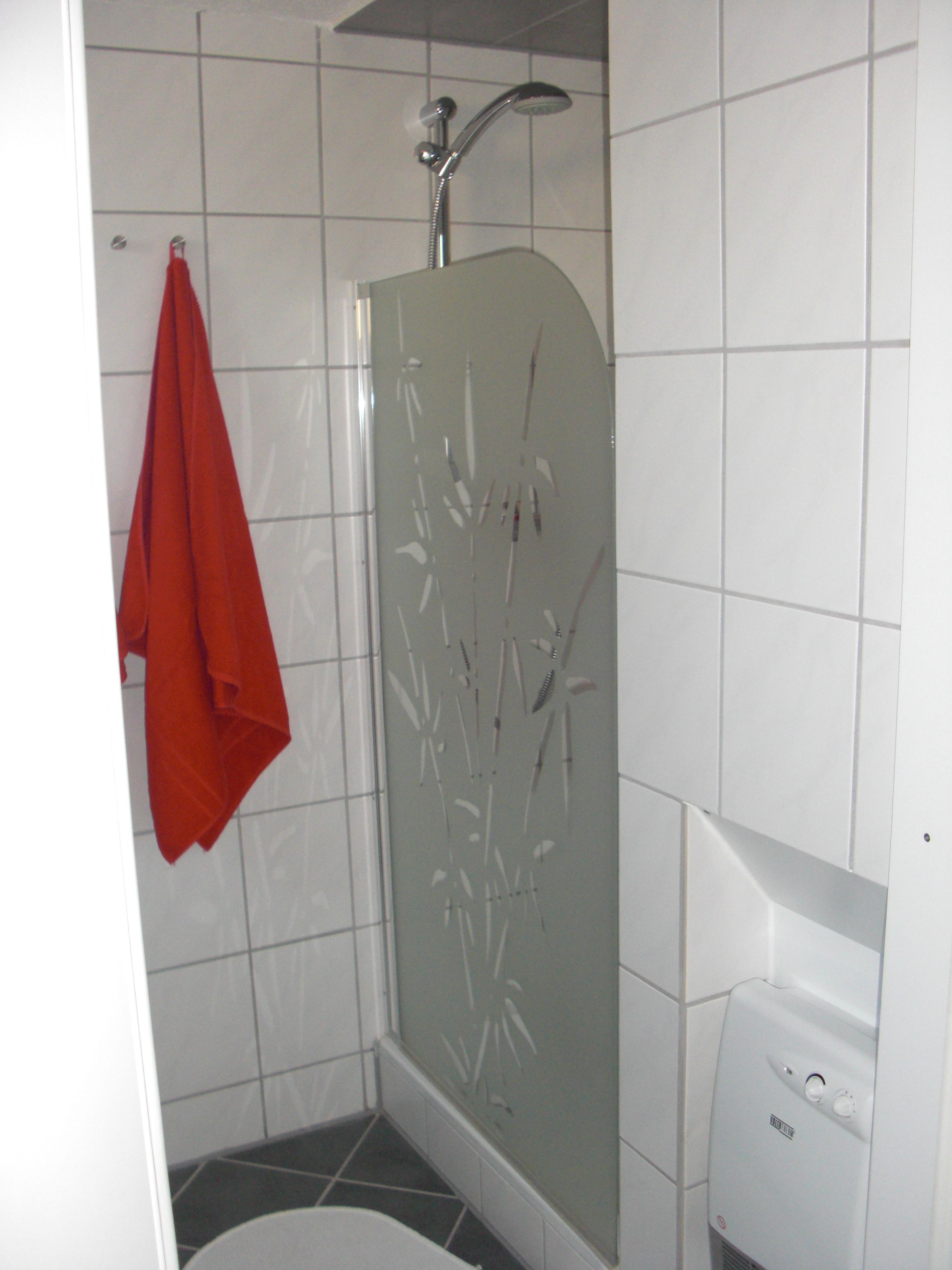 A bathroom with a shower, a red towel hanging on the wall, and a white sink.