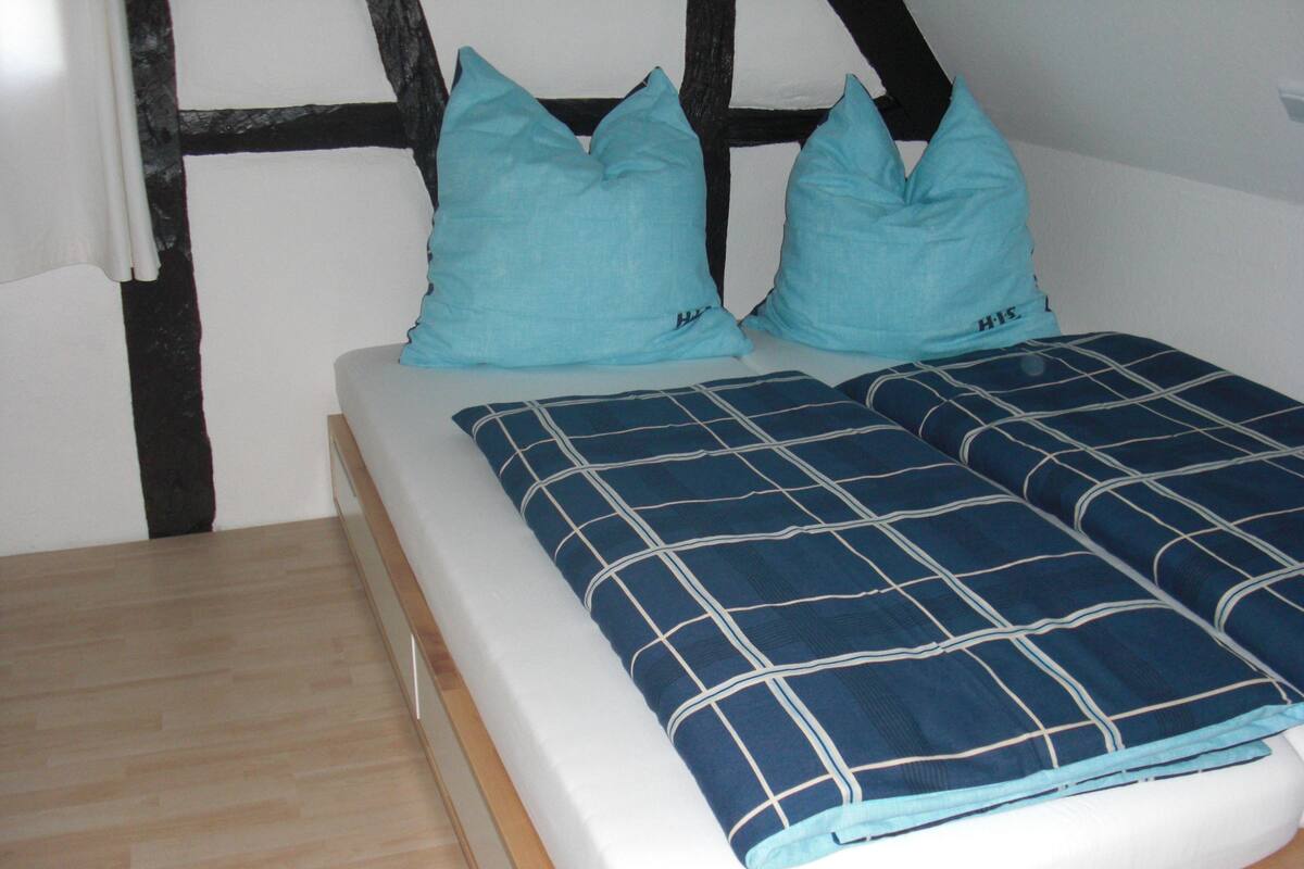 A bed with a blue and white checkered bedspread, two matching pillows, and a wooden nightstand.