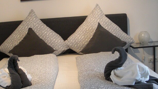 Una cama con almohadones estampados, un almohadón decorativo con forma de cisne y un cuadro de un muelle.