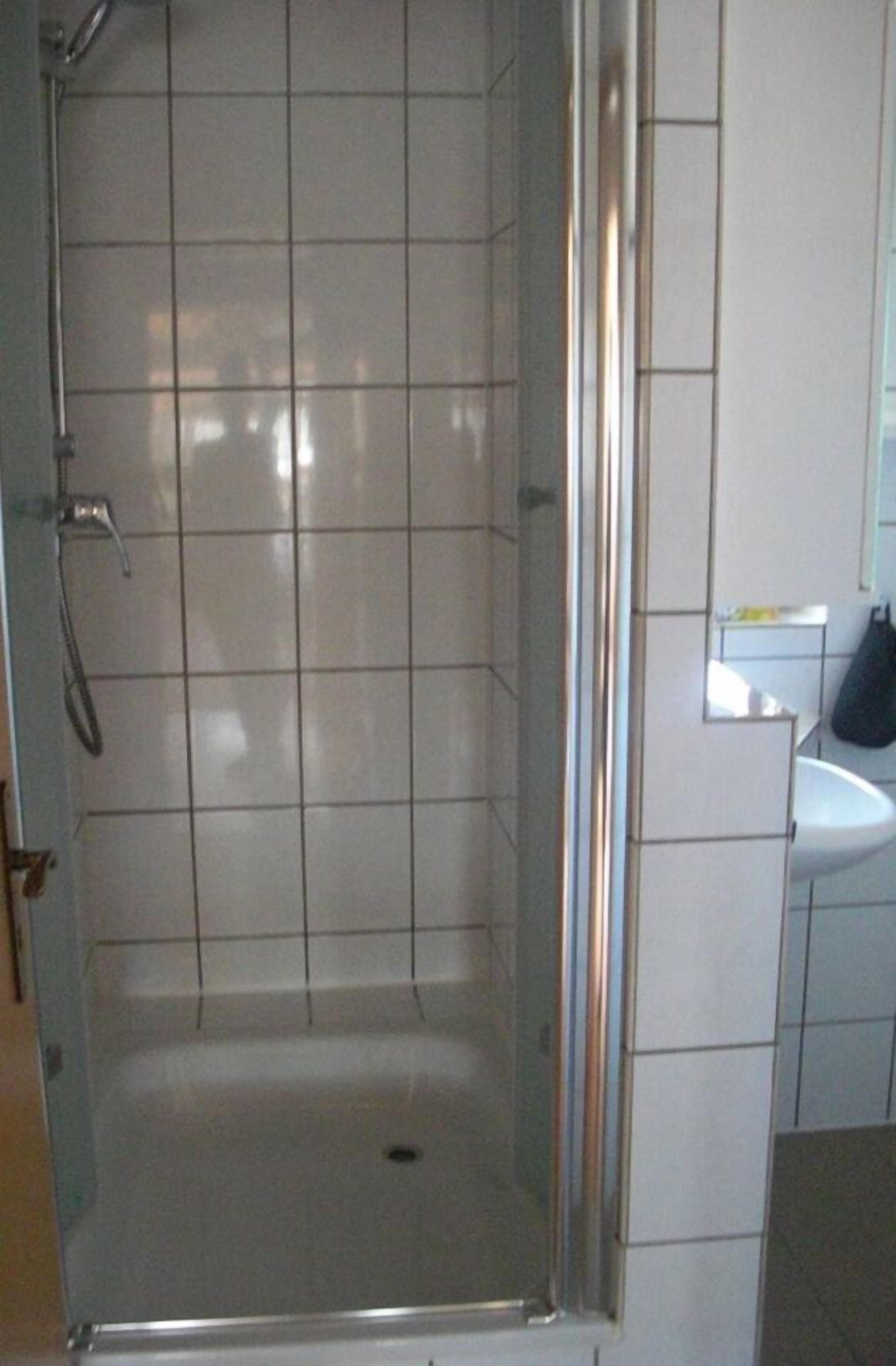 Ein Duschbereich mit Glastür, geflieste Wände und ein weißes Waschbecken im angrenzenden Raum.