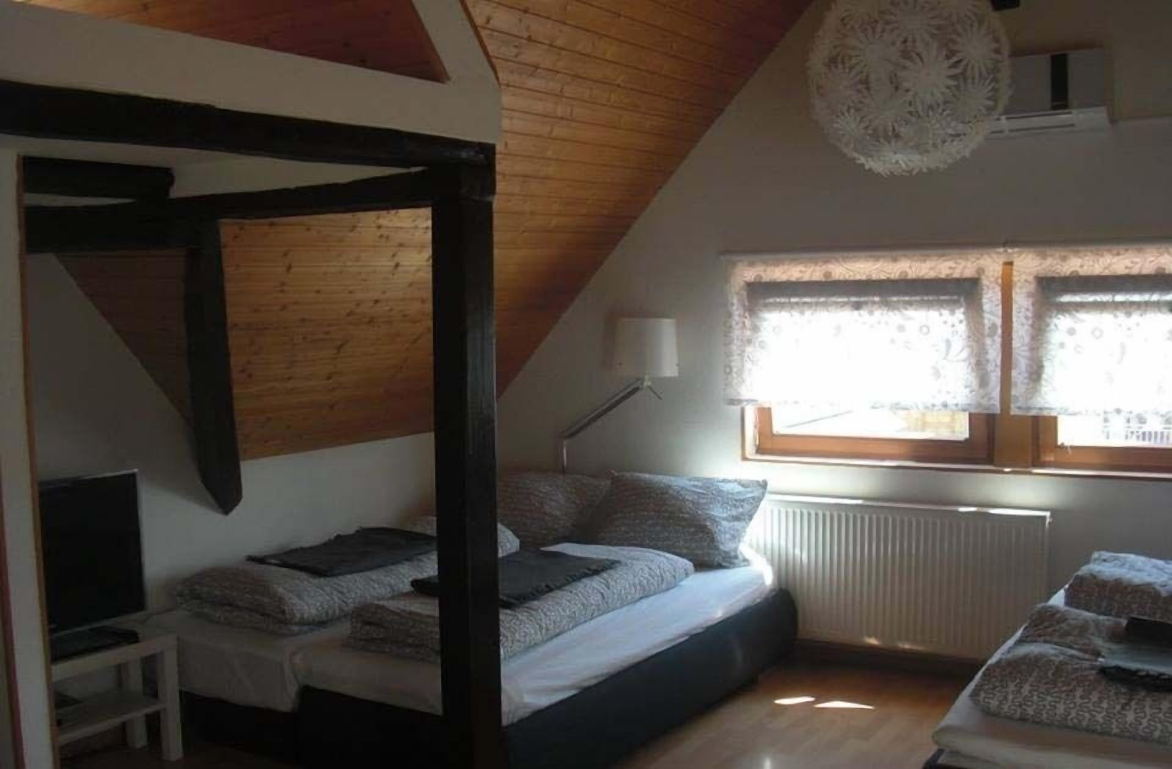 A bedroom with a sloped ceiling, a bed, a bedside table, a lamp, and a window with lace curtains.