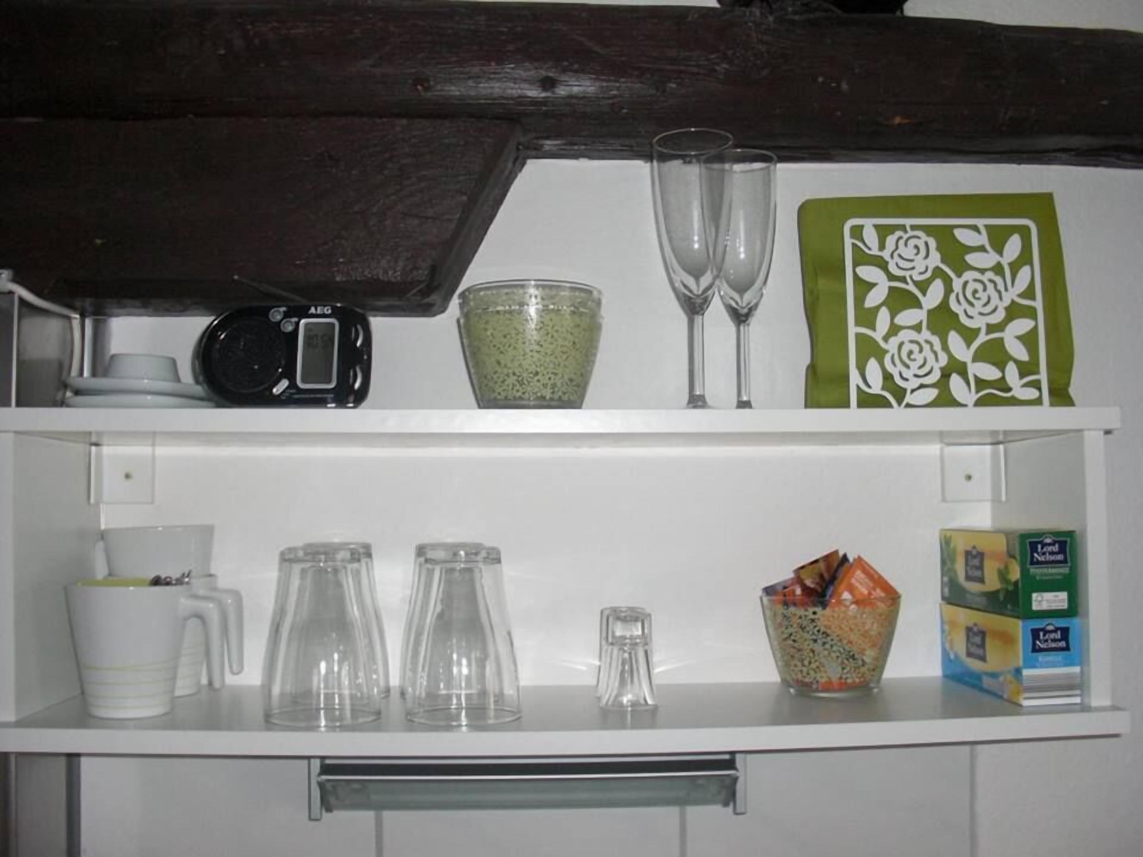 A kitchen counter with various items including a scale, a bowl of green grains, two wine glasses, a coffee maker, and a box of tea.