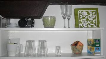 A kitchen counter with various items including a scale, a bowl of green grains, two wine glasses, a coffee maker, and a box of tea.