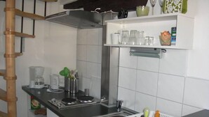 Una cocina con estufa, pileta y estanterías con cristalería y utensilios de cocina.