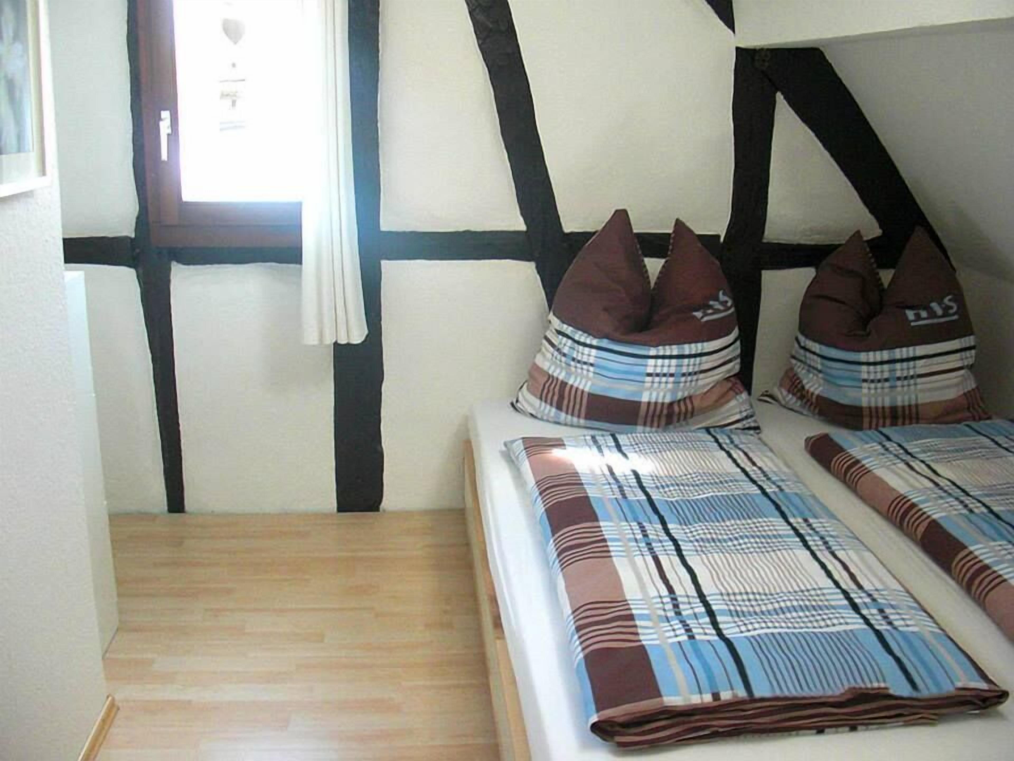 A bedroom with a wooden floor, a bed with plaid bedding, and a window with curtains.