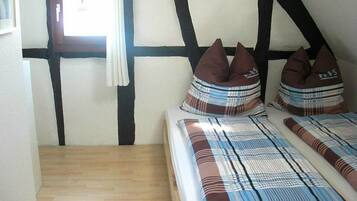 A bedroom with a wooden floor, a bed with plaid bedding, and a window with curtains.