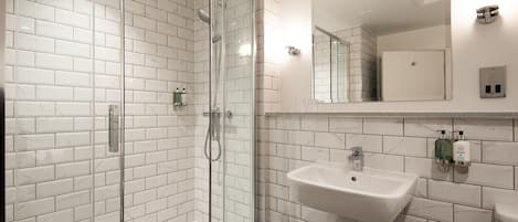 A modern bathroom with white subway tiles, a glass-enclosed shower, a white sink, and a mirror above it.