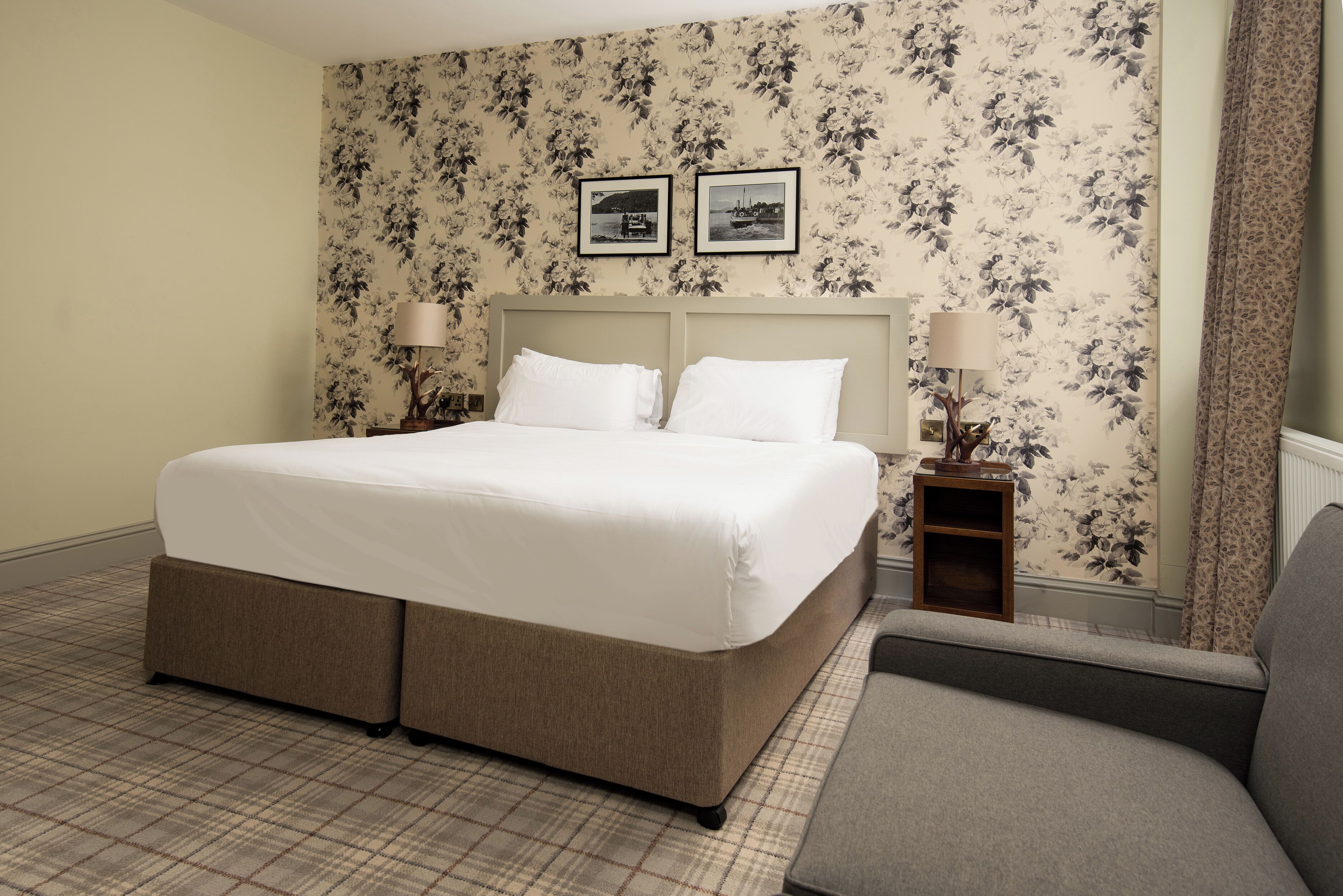 A neatly made bed with a headboard, two bedside tables with lamps, and a floral-patterned wallpaper.