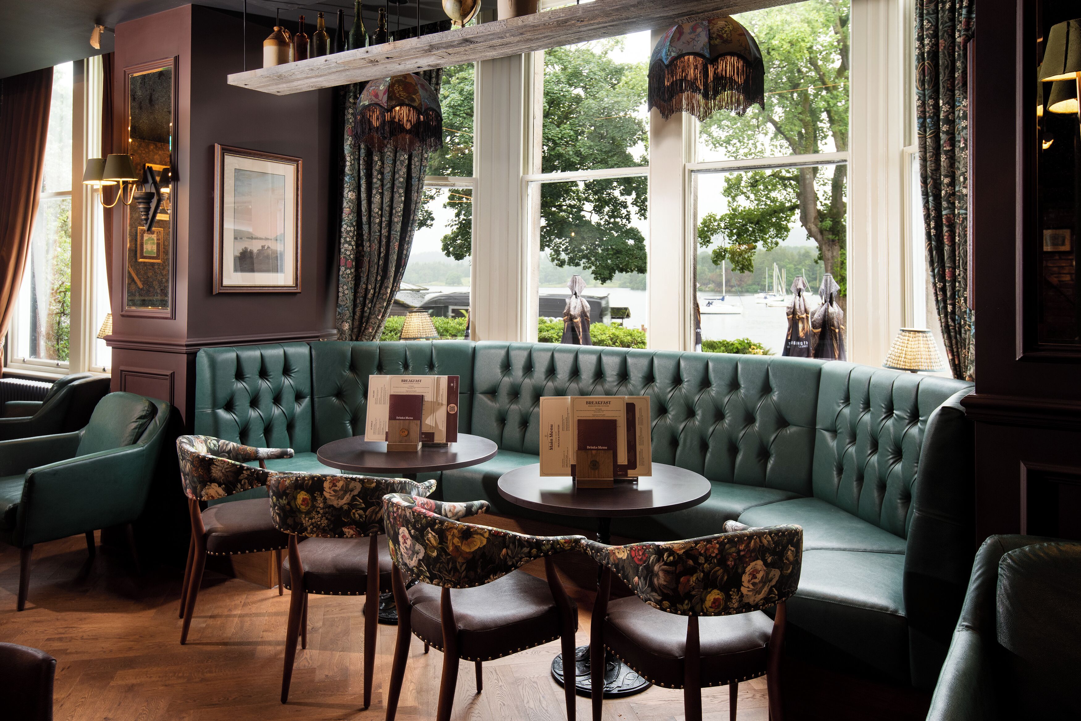 A green upholstered sofa with a tufted backrest, surrounded by floral-patterned chairs, and a round table with a box on it.