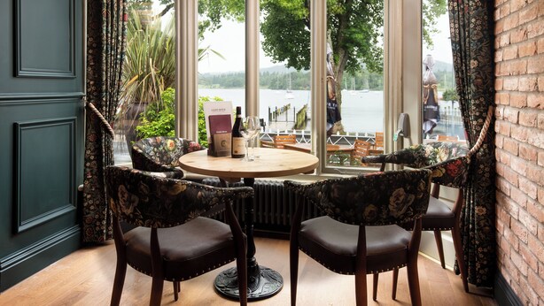 A dining area with a round table and four chairs, a view of a lake with boats, and a brick wall. - The Waterhead Inn - The Inn Collection group (Ambleside)