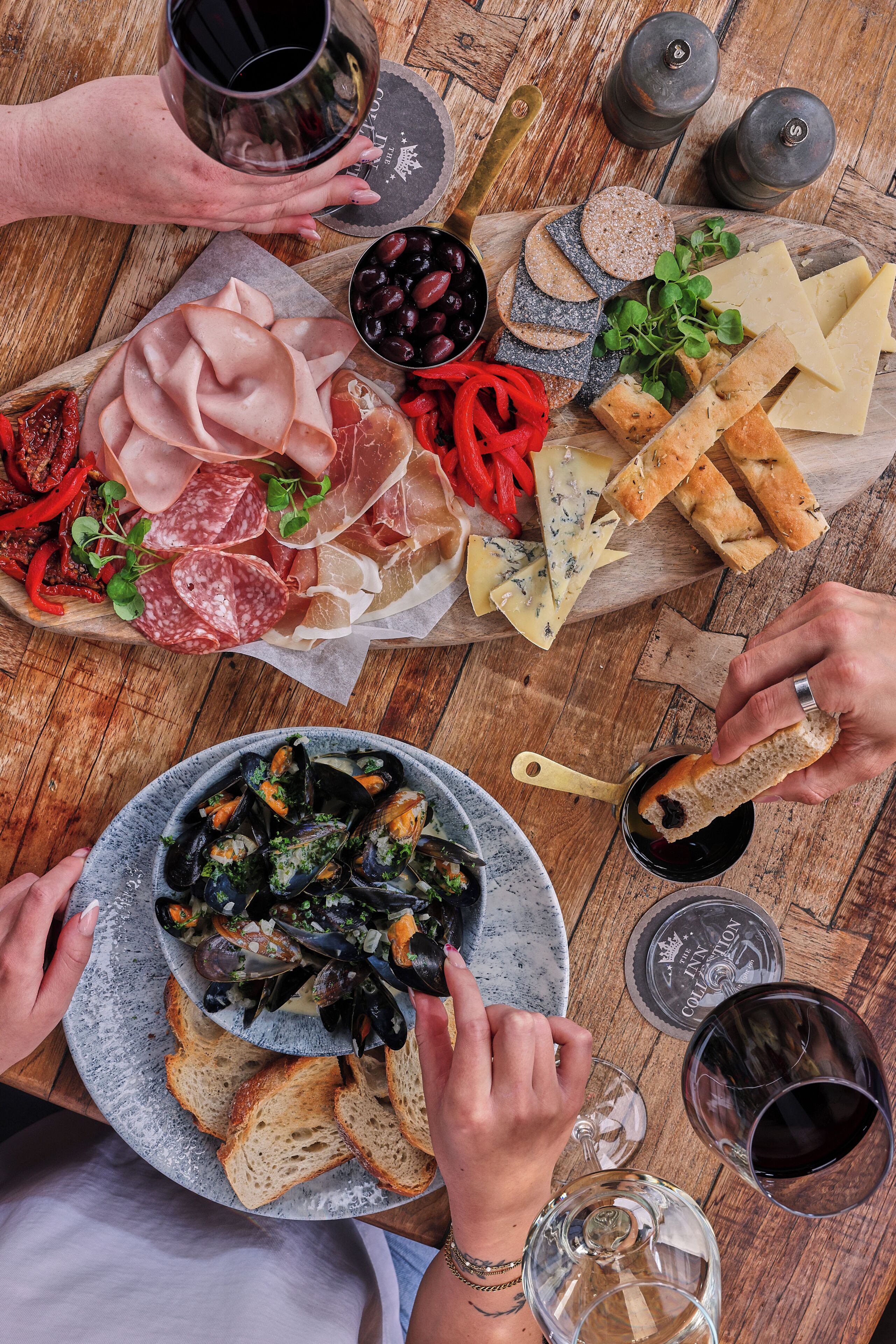 A wooden table with various food items and drinks, including cheese, meats, olives, and bread.