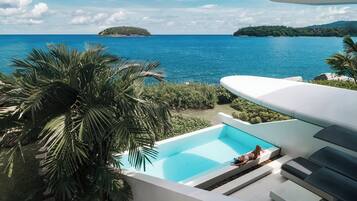 A pool with a view of the sea, surrounded by palm trees and a white structure.