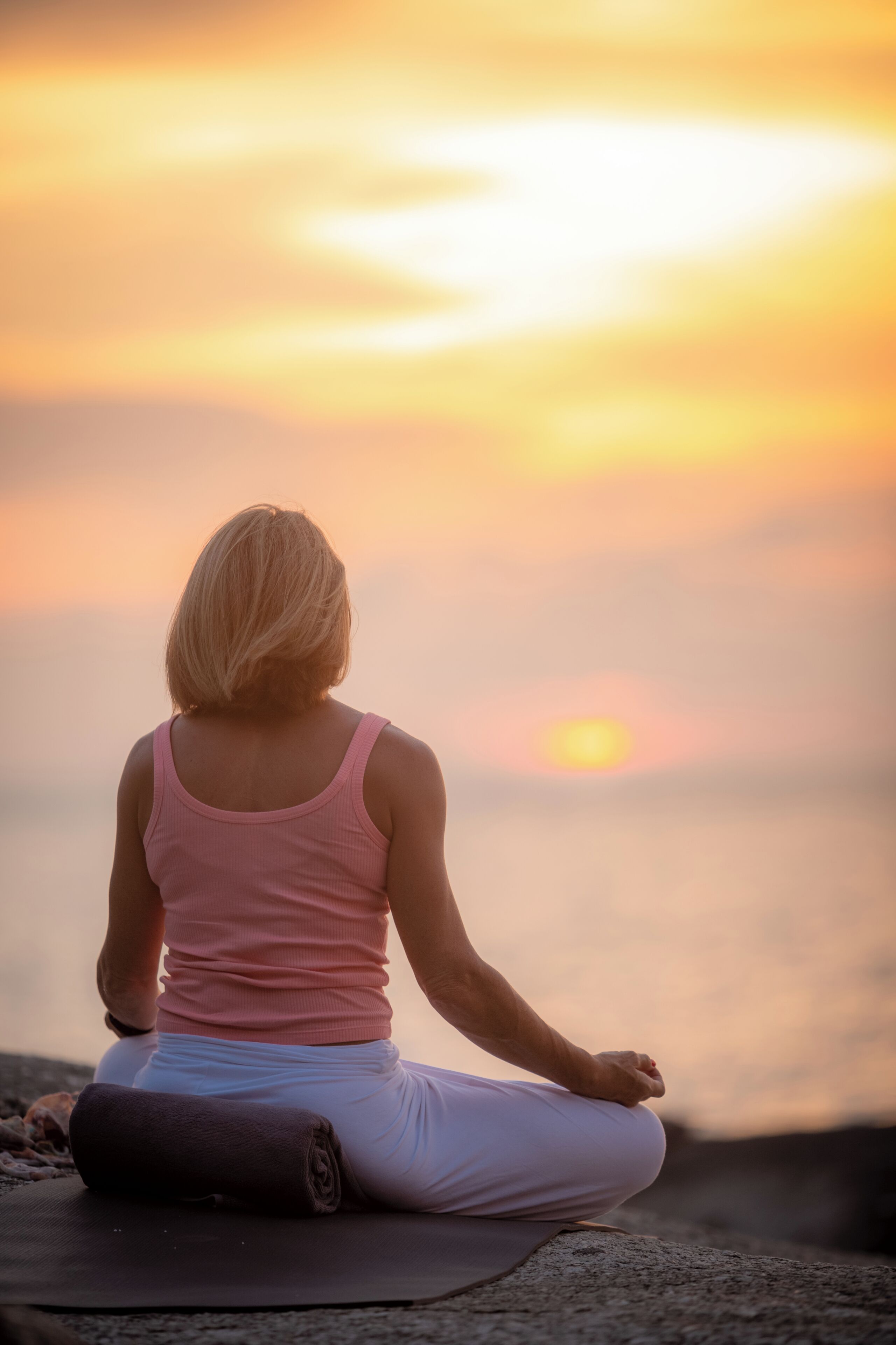 Une personne assise sur un tapis à l’extérieur, avec un coucher de soleil en arrière-plan.
