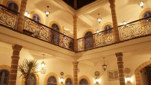 Un hall de hotel con un atrio central, que presenta una palmera, puertas arqueadas y barandillas decorativas de hierro.