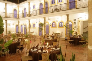 A spacious indoor dining area with multiple tables set for guests, featuring a classic architectural design with arched windows and a balcony. - Hotel Villa Damonte (Essaouira)