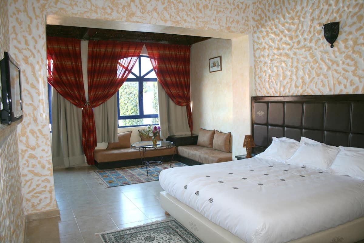 A bedroom with a large bed, a sofa, a small table, and a window with curtains.