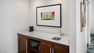 A kitchenette with a microwave, sink, and cabinet, a framed picture on the wall, and a patterned carpet.