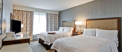 A hotel room with two beds, a desk, a TV, and a window with curtains.