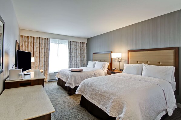 A hotel room with two beds, a desk, a TV, and a window with curtains. - Hampton Inn & Suites Detroit/Troy (Troy)