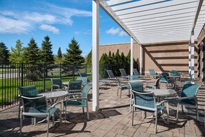 An outdoor patio with chairs and tables, a covered area, and a brick building in the background. - Hampton Inn & Suites Detroit/Troy (Troy)