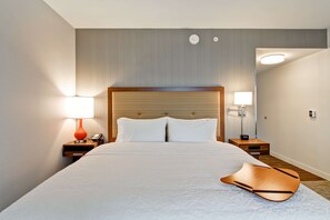 A hotel room with a large bed, two bedside tables, a nightstand, a lamp, and a wall-mounted light. - Hampton Inn & Suites Detroit/Troy (Troy)