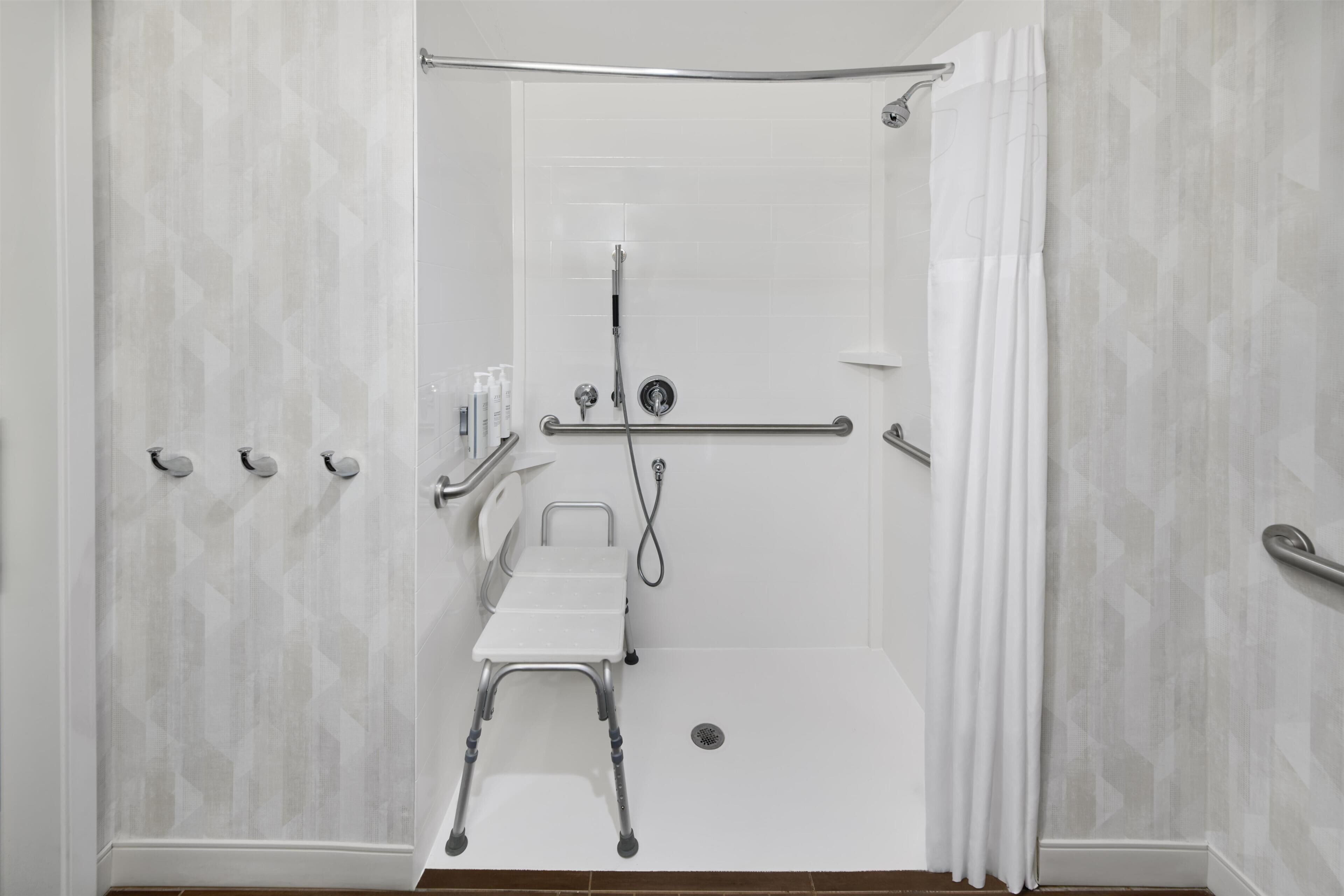 Eine bodenebene Dusche mit Haltegriff, einem weißen Stuhl und einer Duschbrause.