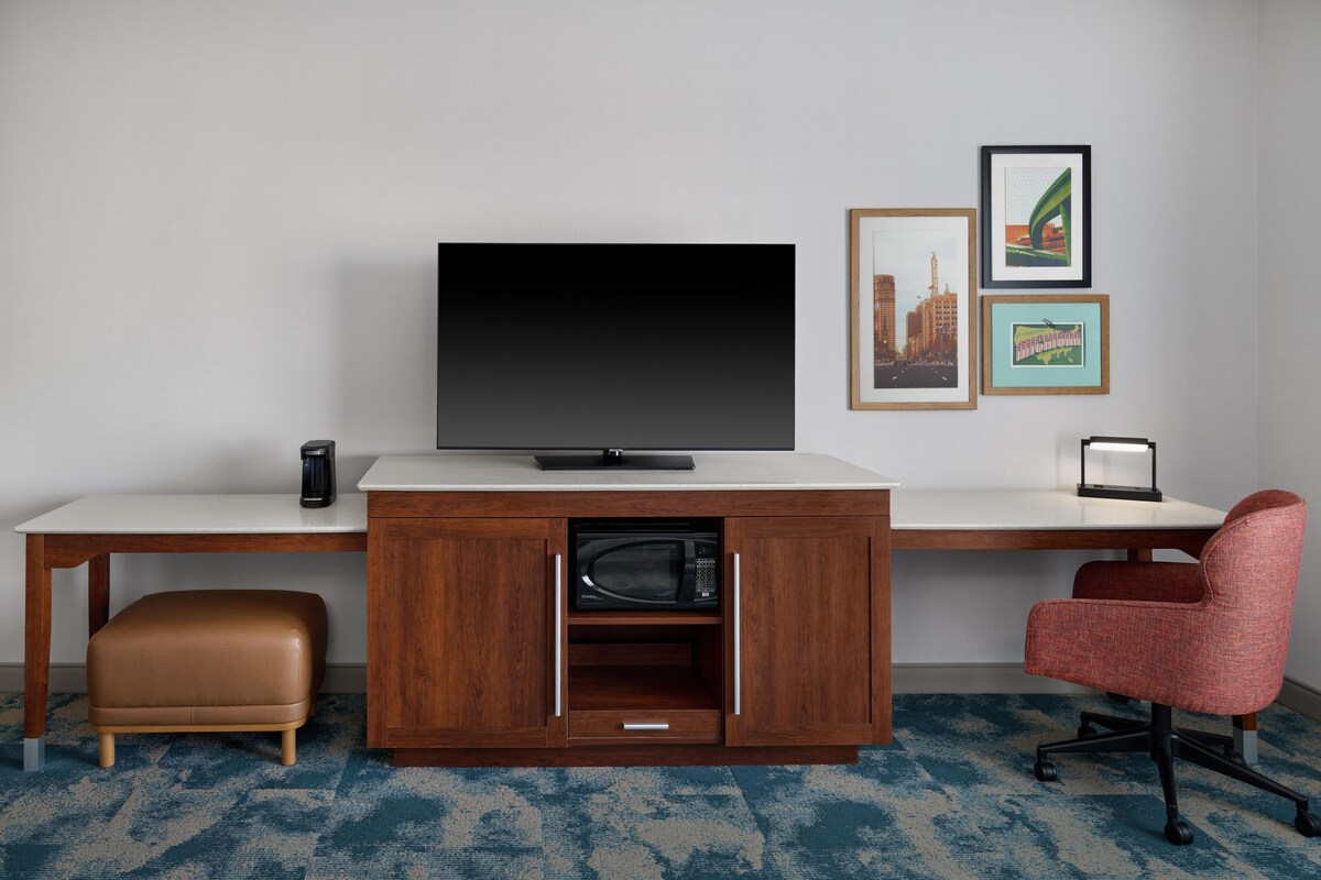 A modern room with a flat-screen TV, a wooden cabinet with a microwave, a red office chair, and framed pictures on the wall.