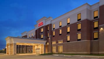 Un hotel con fachada de ladrillo, un acceso cubierto y un cartel que indica que es un Hampton Inn.