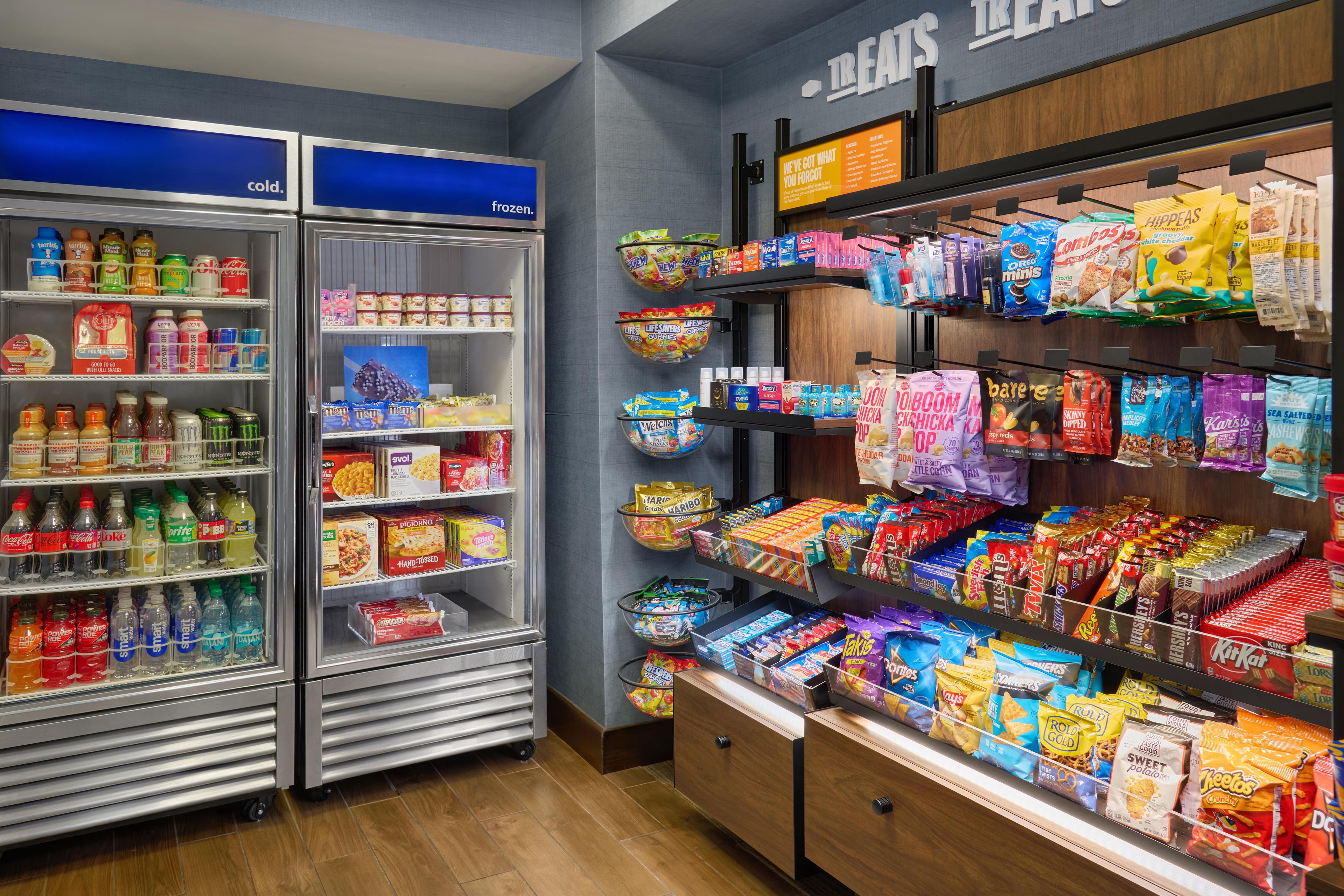 Un rayon réfrigéré proposant diverses boissons et en-cas, un rayon surgelés avec des glaces et des produits surgelés, et des étagères remplies d’en-cas et de chocolats emballés.