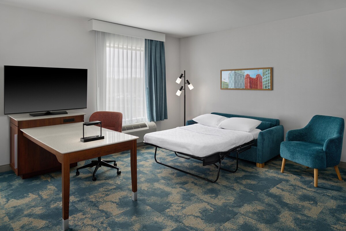 A hotel room with a bed, a desk, a chair, a TV, and a window with curtains.