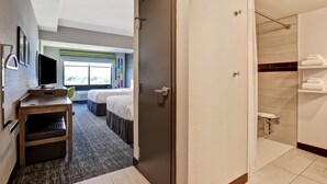 A hotel room with a bed, a desk with a computer, a TV, a bathroom with a shower, and a window with a view of trees. - Hampton Inn & Suites Huntsville (Huntsville)