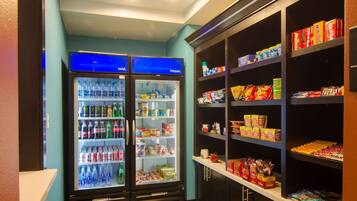 Una máquina expendedora con diversas bebidas y aperitivos, y estantes repletos de productos envasados.