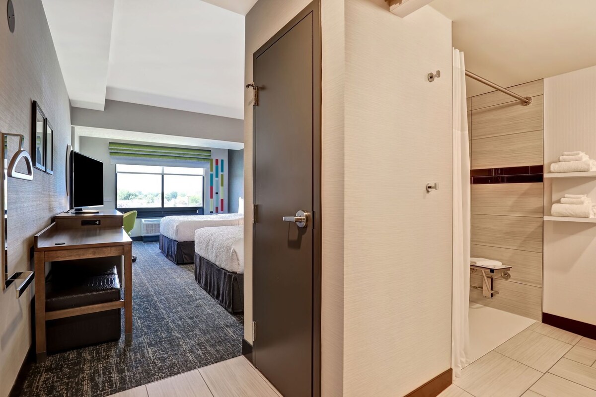 A hotel room with a desk, two beds, a shower, and a view of the outdoors.