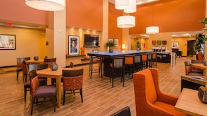 A restaurant with a bar area, multiple tables, and chairs. There are hanging lights, a trash can, and a waste bin. - Hampton Inn & Suites Huntsville (Huntsville)